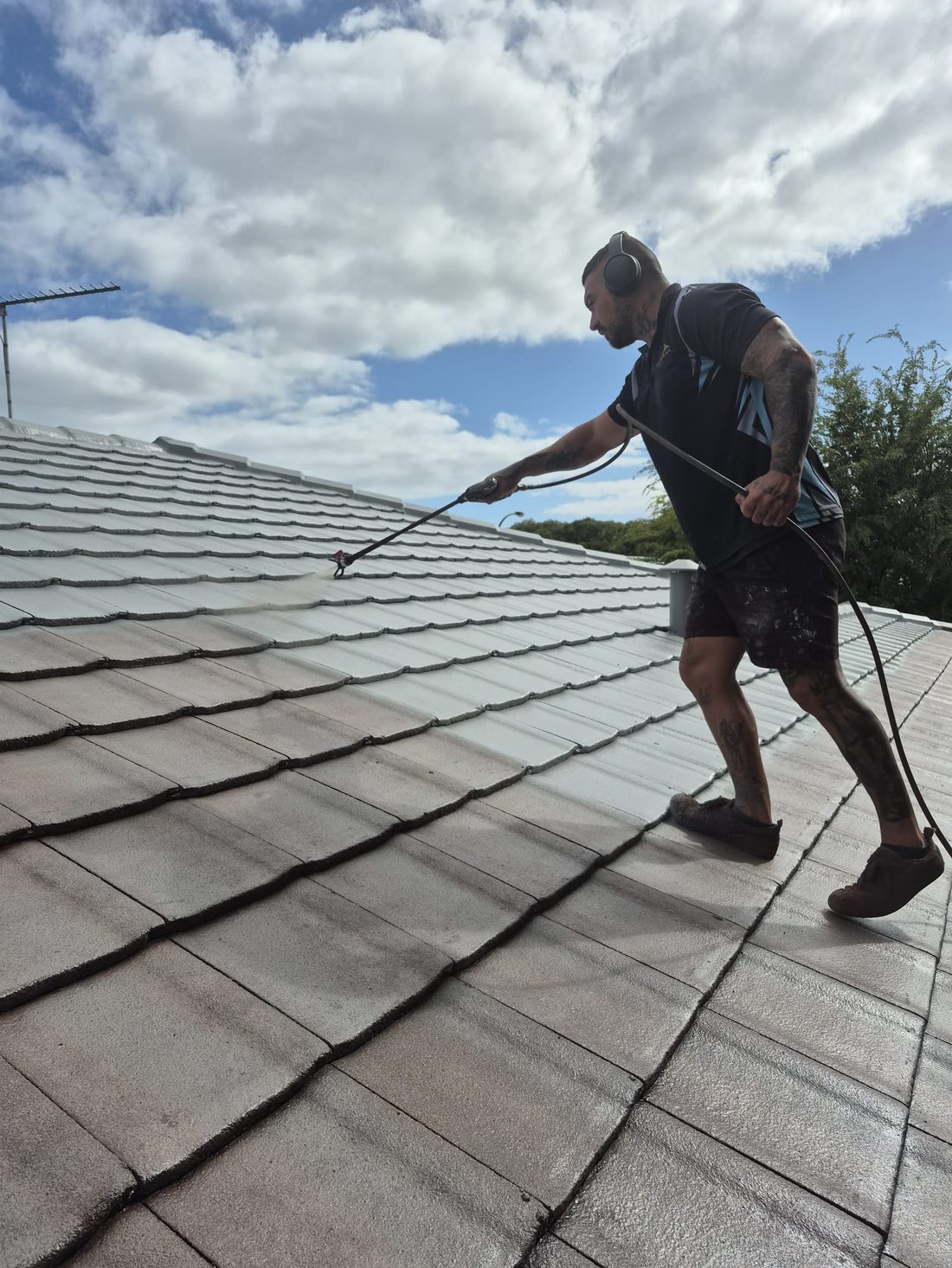 Spraying a fresh coat along a tile roof, working back across the ridge