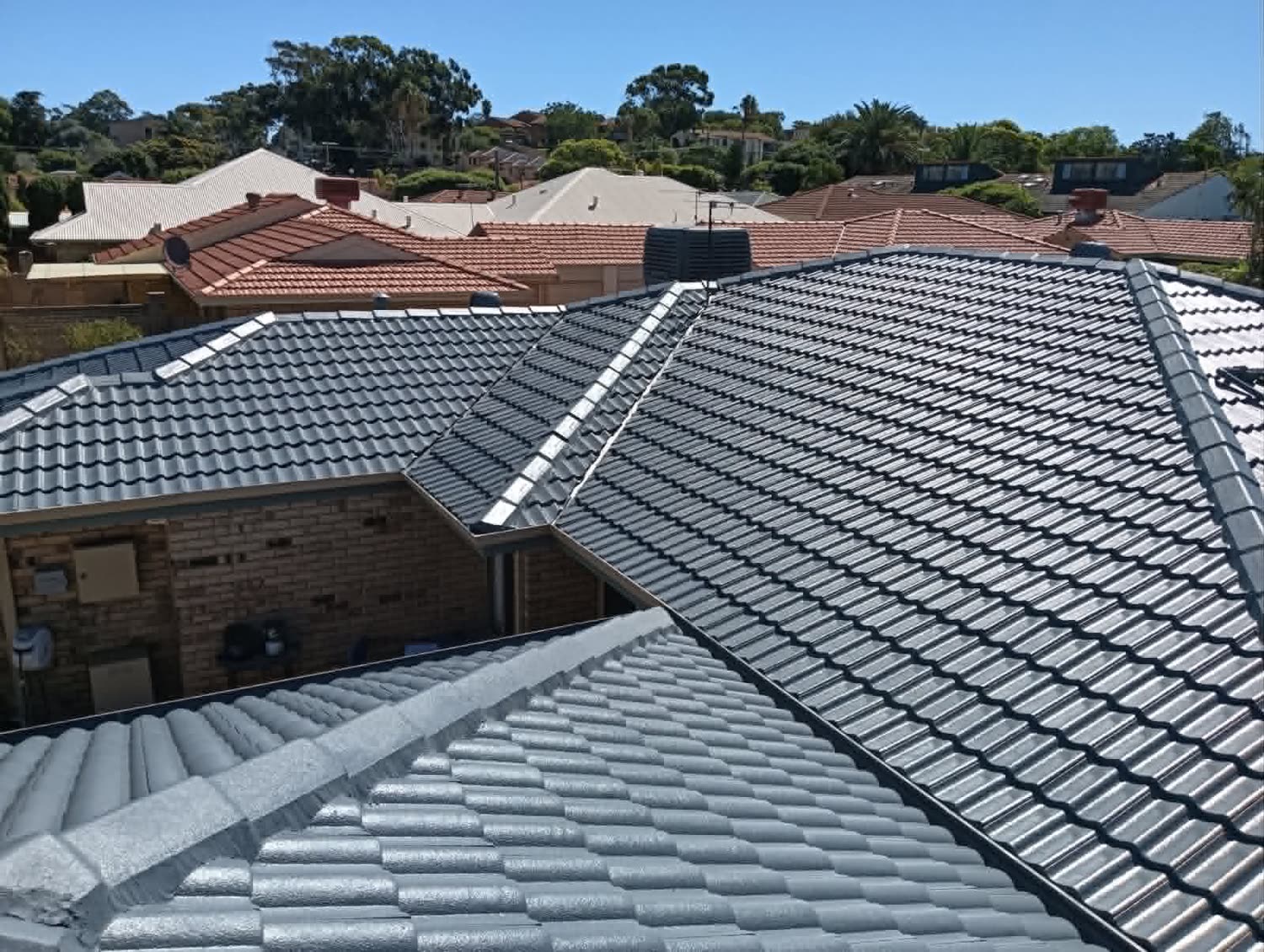 After: the same tile roof in its finished charcoal coat, ridge caps and valleys uniform