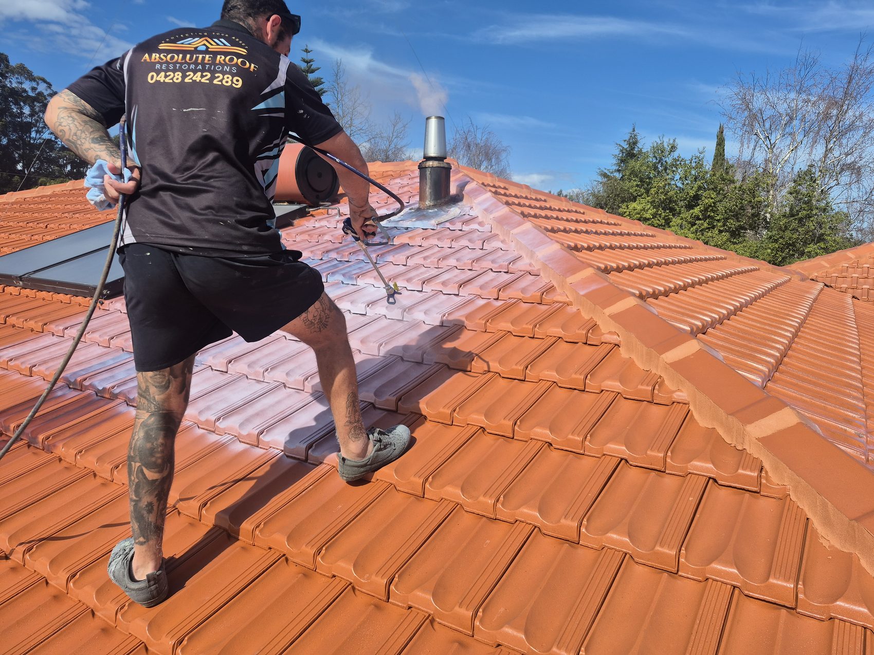 Jake spraying a fresh terracotta coating across a restored tile roof